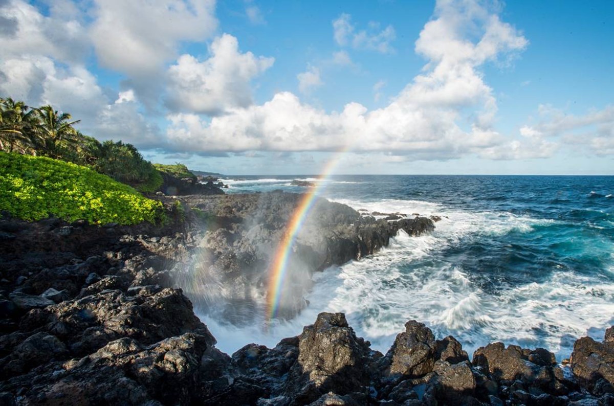 A rainbow forms in the mist of the ocean crashing on a rocky shore on Hawaii's island of Maui. Image: NPS / Chris Archer
