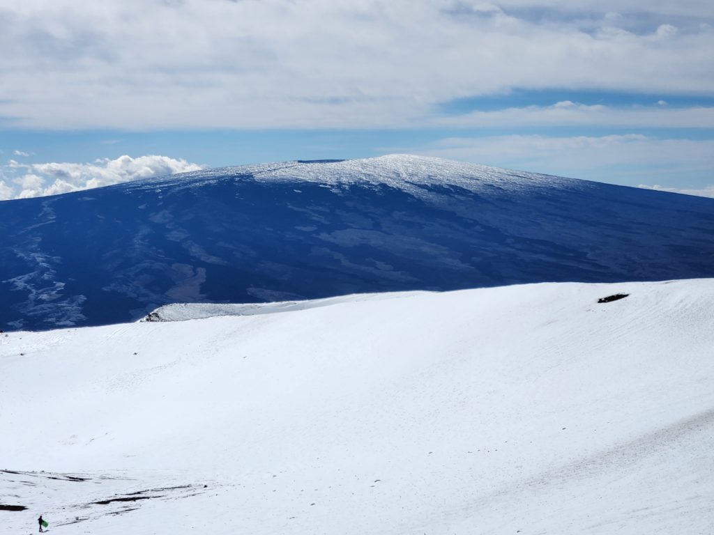 Deep snow covers the summit region of Mauna Kea while Mauna Loa is also snow-capped in the background. Note the snowboarder in the bottom left of this picture for a reference to how vast this area is. Image: Weatherboy