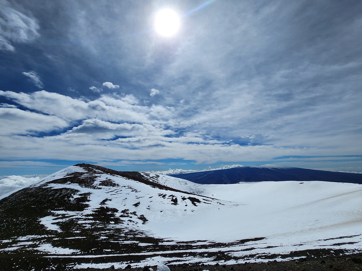 The summit of Mauna Kea is under the sun to the left, while snow-capped Mauna Loa, where lava was flowing down just weeks ago, stands in the background. Image: Weatherboy