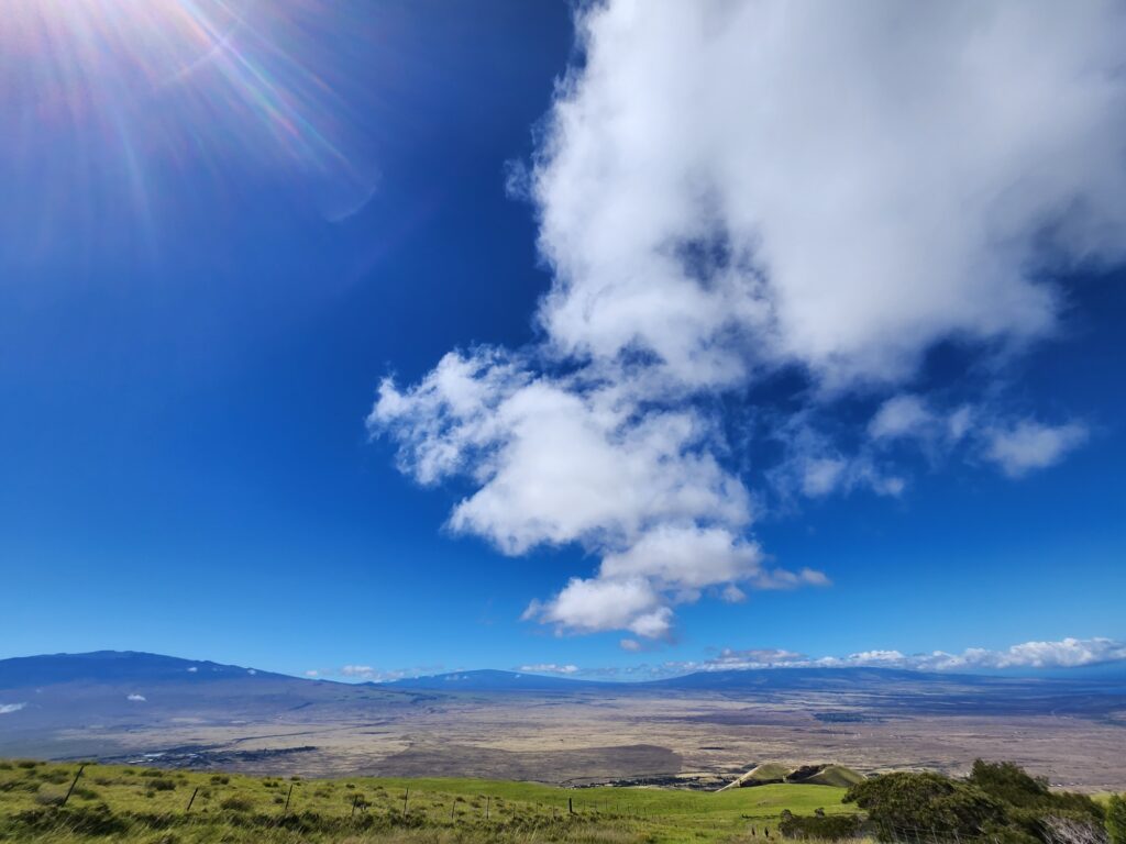 During typical trade winds on the Big Island, winds flowing out of the east pass through the "saddle" region that exists between Mauna Kea, left, and Mauna Loa, right, blowing fast moving, generally dry air into the communities of South Kohala. Hualalai Volcano, capped in clouds here to the right, obstruct the wind flow from doing the same to Kailua-Kona further south on the coast. Image: Weatherboy